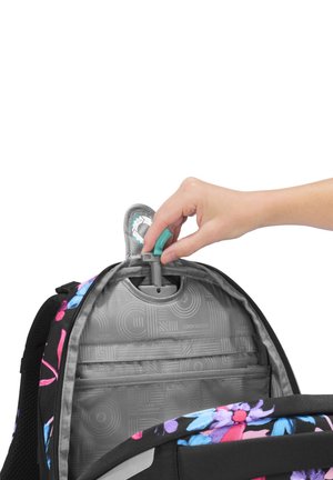 Hand adjusting gray carrying handle inside open black backpack with colorful floral pattern and gray interior lining.