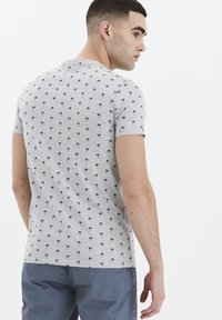 Grå kortærmet t-shirt med et sort palme-mønster, rund hals og slim fit. Kombination med mørkeblå shorts.
