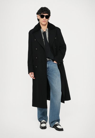 Abrigo largo negro con diseño de doble botonadura, textura de lana, cuello grande, combinado con una camisa negra y vaqueros anchos de pierna en azul claro. Zapatos negros.