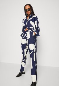 Navy and white patterned button-up shirt and matching pants, made of smooth fabric. The shirt features a collar and relaxed fit. Black sunglasses.