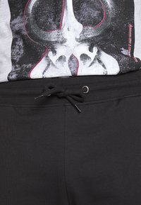 Pantalones jogger negros con una cintura elástica y cordón ajustable. La tela es suave, con un diseño casual apto para un uso relajado.