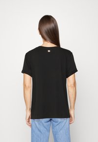 Camiseta negra de manga corta con cuello redondo y mangas enrolladas, que presenta un pequeño detalle de logo en relieve en la parte posterior del cuello.