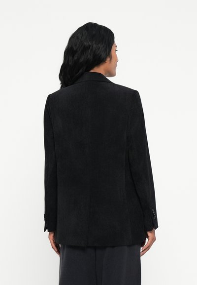 Blazer en velours côtelé noir avec une coupe ajustée, des revers à cran et une fente arrière simple, accompagné de détails en bouton sur les manches.