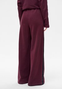 Bordeauxrode broek met wijd uitlopende pijpen van gladde stof, met mesh accenten aan de zijkant en een elastische tailleband voor een comfortabele pasvorm.