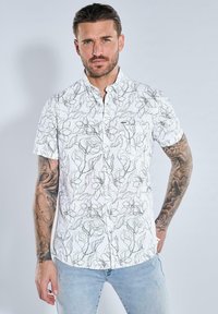 Weißes Kurzarmhemd mit schwarzem Blumenmuster, Button-Down-Kragen und einer Taschenapplikation. Der Stoff wirkt leicht und strukturiert.