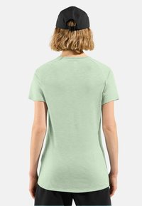 Light green short-sleeve T-shirt with a rounded hem and raglan sleeves, paired with a black cap featuring an adjustable back strap.
