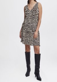 Robe sans manches à imprimé léopard avec un décolleté en V, design superposé, en tissu léger, assortie à des bottes noires à talons jusqu'aux genoux.