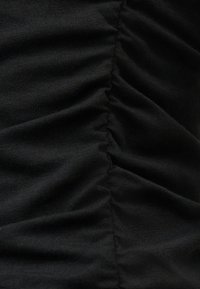 Κοντινή λήψη μαύρου υφάσματος με μια κεντρική κάθετη ραφή που δημιουργεί μαζεμένη, ρυτιδωτή υφή.