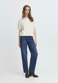 Crème trui met korte mouwen en een boxy pasvorm, gecombineerd met blauwe recht model jeans en zwarte haklaarzen. Eenvoudig ontwerp, geen patronen.