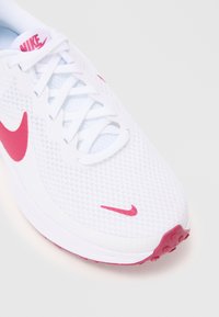 Witte sportieve schoen met een gestructureerde bovenkant, roze Nike swoosh en roze accenten op de zool. Voorzien van witte veters en ademend mesh-materiaal.
