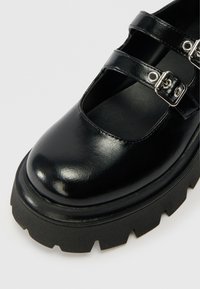 Shoe Mary Jane em couro preto com bico arredondado, detalhes de duplo fecho e solado de borracha espessa e serrilhada. Acabamento suave com textura brilhante.