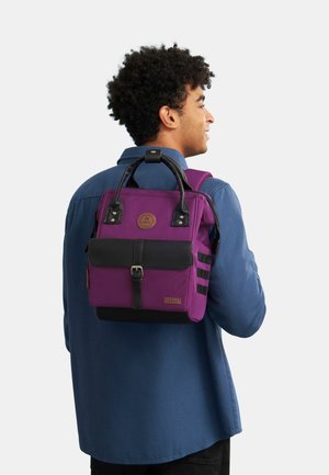 Sac à dos violet avec accents noirs, forme rectangulaire, fermeture à rabat à l'avant, détails en cuir et rayures latérales. Bretelles réglables pour le confort.