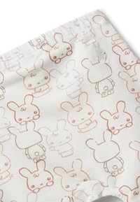 Bílá tkanina s opakujícími se jednoduchými obrysy postavy králíka v světle hnědé a béžové, někteří čelí vpředu a jiní vzadu, malý vyšívaný detail králíka.