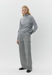 Pelēks zābaksvītra džemperis, izgatavots no mīksta adījuma auduma, apvienots ar platām svītrainām biksēm pelēkos un baltos toņos. Melni apavi noslēdz apģērbu.