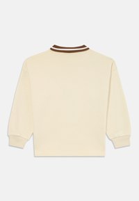 Camicetta beige a maniche lunghe con polsini a coste e colletto a coste a righe marroni e bianche, vista dal retro su uno sfondo bianco.