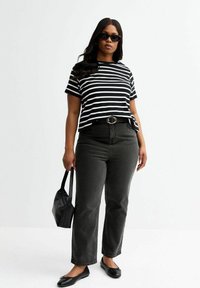Randig topp med korta ärmar i svart och vitt, tillsammans med högmidjade svarta jeans och svarta ballerina skor. Tillbehör inkluderar en svart handväska och solglasögon.