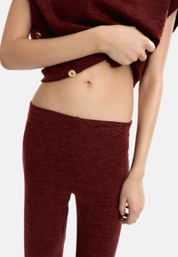 Burgundowy sweter z dzianiny z guzikami oraz dopasowane spodnie. Miękka tekstura, fason podkreślający sylwetkę, eksponujący środkową część brzucha.