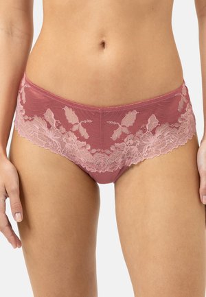 Femme portant une culotte hipster en dentelle mauve, montrant la section médiane et le haut des cuisses sur un fond uni.