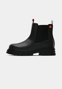 Botas Chelsea negras de cuero con paneles laterales elásticos, punta redonda, suela de goma gruesa y acentos rojos y naranjas en el talón.