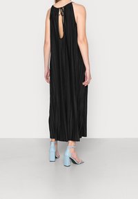 Černé plisované maxi šaty s otevřením na zádech, které jsou zajištěny šňůrkami. Nosené s jasně modrými lakovanými sandály na blokovém podpatku.