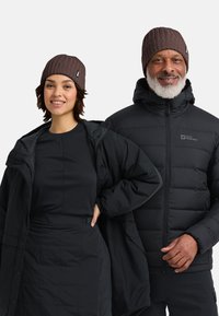 Bruine geribde beanie, zwarte geïsoleerde pufferjack en een zwarte top met een gestructureerde rok; minimalistisch ontwerp, geschikt voor koud weer.