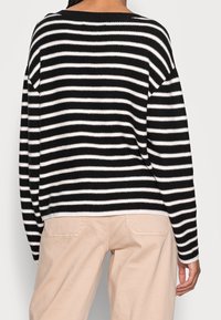 Černobílý pruhovaný svetr s volným střihem, širokým výstřihem a dlouhými rukávy, kombinovaný se světle béžovými kalhotami. Pletená texturovaná látka.