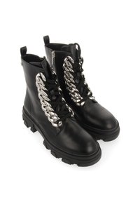 Botas de cuero negras hasta el tobillo con suela gruesa, con un detalle de cadena plateada brillante en la parte frontal y cordones negros. Incluye cierre de cremallera lateral.