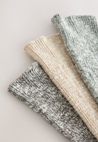 Trois jambières en tricot de couleur gris, crème et vert clair. Motifs texturés avec poignets côtelés et fil doux et épais pour la chaleur.