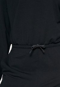 Vêtement en tissu noir avec une ceinture à cordon nouée et des coutures visibles sur le devant et les côtés.