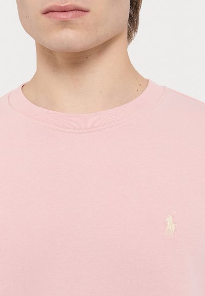 Lyserød bomulds sweatshirt med ribbet rund hals og et lille, broderet logo i hvidt på venstre bryst. Glat tekstur.