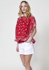 Top in cotone rosso con stampa paisley e design svasato, abbinato a pantaloni corti in cotone bianco di vestibilità comoda. Maniche corte, senza chiusure.