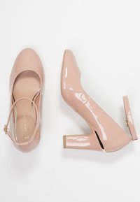 Rosa lackläder högklackade skor med rund tå, ankelrem och en klack med blockform och guldaccent. Slät yta och minimalistisk design.