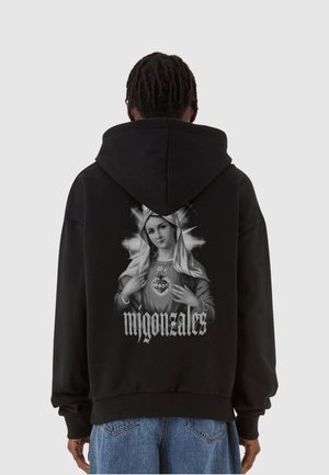 Schwarzer Hoodie mit einem großen Grafikdruck einer Frau, die ein Herz hält, und dem Text "m gonzales" darunter. Entworfen mit einer geräumigen Kapuze.