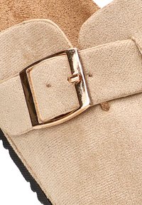 Sandalia de ante beige con un hebilla metálica en tono dorado y una suela texturizada. El diseño incluye una tira ancha y una plantilla contorneada.