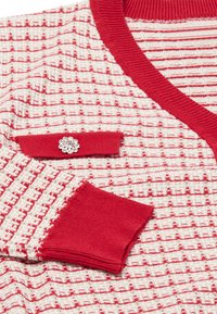 Rot-weißer, gemusterter Cardigan mit geripptem Kragen und Bündchen. Verfügt über eine dekorative, blumenförmige Verzierung auf der Brusttasche.
