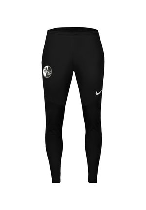 Sorte atletikbukser med hvidt Nike-logo på højre lår og et rundt sort-hvidt sportsholds emblem på venstre lår.