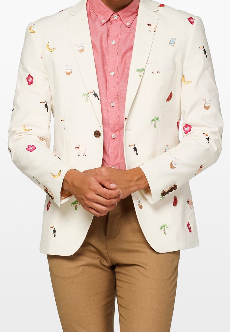 Biała, haftowana marynarka z kolorowymi motywami, takimi jak banany i kwiaty. Nosi ją na różowej koszuli z guzikami i beżowych spodniach.