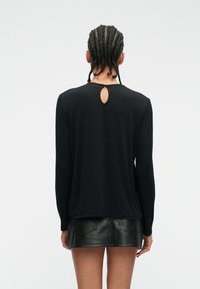 Top negro de manga larga con textura acanalada, que presenta un detalle de ojal en la parte posterior del escote. Combinado con una falda mini de cuero.