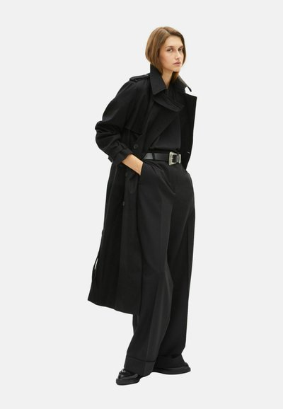 Czarny płaszcz trench, o oversize'owym kroju, z wysokim kołnierzem i guzikami. W połączeniu z szerokimi czarnymi spodniami i eleganckimi butami.