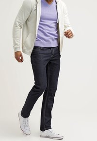 Lichtgrijze zip-up hoodie, lilac V-hals T-shirt, donkerdenim jeans en witte sneakers. Casual outfit met capuchon en zakken.