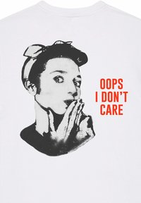 T-shirt en coton blanc avec une illustration monochrome d'une personne portant un arc. Le texte indique "OUPS, JE M'EN FOUS" en police rouge en gras.