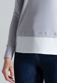 Grijze lange-mouwen top met een witte onderlaag, voorzien van een zachte textuur en rechte zoom, gecombineerd met donkerblauwe denim.