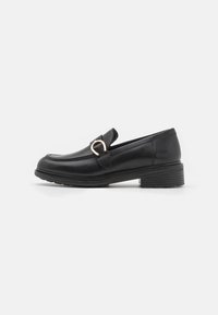 Mocasines de cuero negro con puntera redonda, una pequeña correa y una hebilla de acento en tono dorado en la parte frontal. Presentan un tacón bajo apilado.