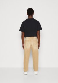 Beiga denimjeans med avslappnad passform, med bakfickor och en subtilt blekt textur, bärs med en svart t-shirt.