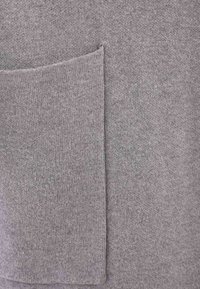 Tissu en tricot gris avec une poche appliquée. La texture est douce avec une apparence légèrement duveteuse. Pas de motifs distincts ni de quincaillerie.