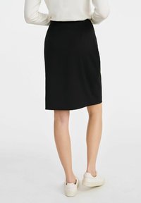 Czarna spódnica do kolan z gładkiego materiału, o prostym kroju i subtelnymi plisami z tyłu. Połączona z białymi trampkami.