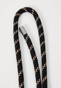 Μαύρο και μπεζ πλεκτό σχοινί με μεταλλικό ασημί κάλυμμα, διαθέτοντας υφή και διαγώνιο σχέδιο κατά μήκος του.