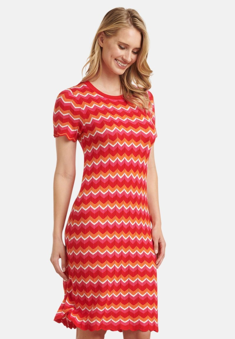 Rotes gestricktes Kleid mit einem Zickzackmuster in Rottönen, Orange und Weiß. Kurze Ärmel, figurnahe Silhouette und knielänger Saum.