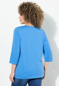 Blaues Langarmshirt mit rundem Halsausschnitt und Dreiviertelärmeln. Aus weichem Stoff gefertigt, hat es einen lässigen Schnitt ohne sichtbare Muster oder Akzente.