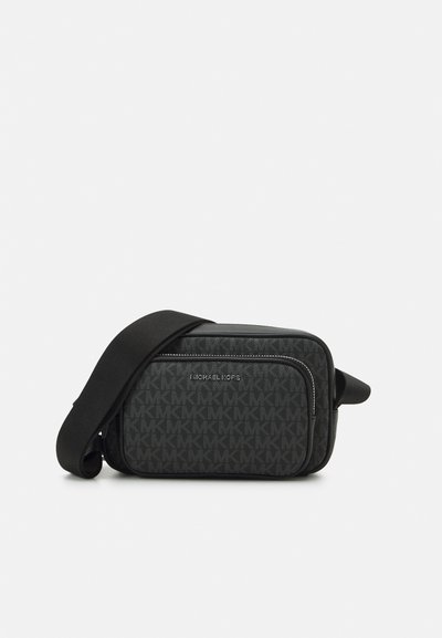 Sac bandoulière noir avec logo MK estampé, poche avant zippée et bandoulière en tissu réglable. Fini en matériau lisse.